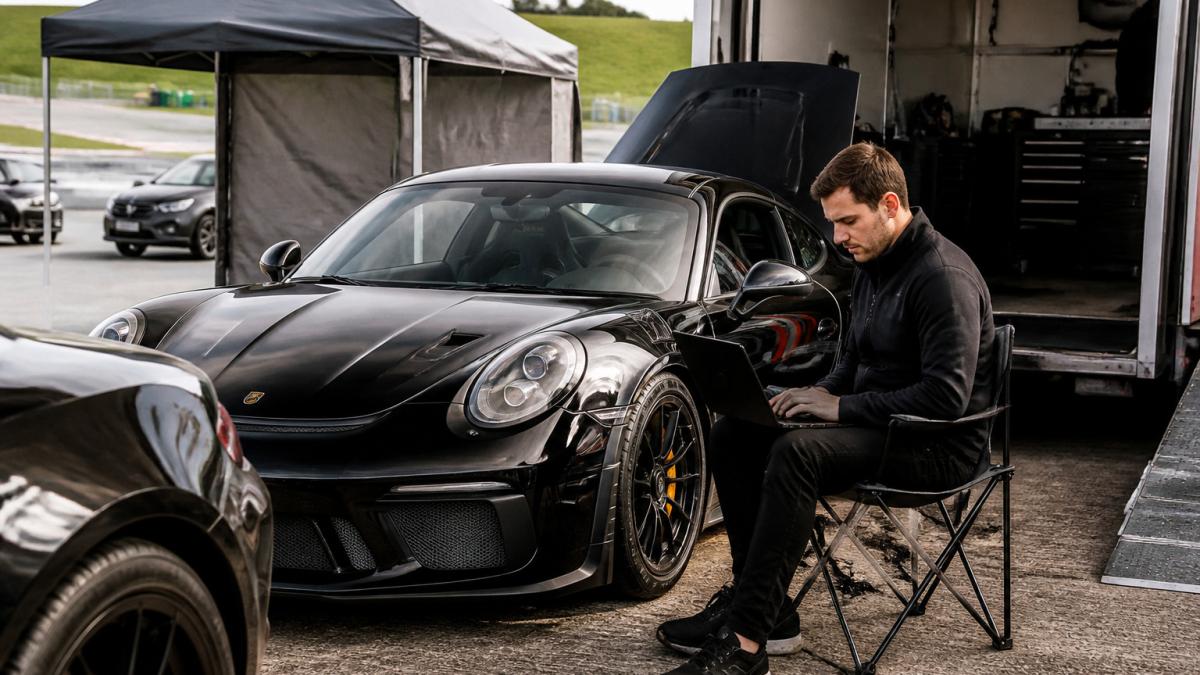 Race engineer using a laptop to calibrate a mileage blocker on a high-performance car at a private circuit paddock